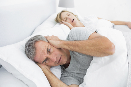 Annoyed man blocking his ears from noise of wife snoring at home in bedroom
